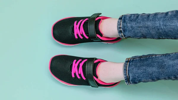 Girl\'s legs in ripped jeans and black and red sneakers on blue pastel background. Fashionable sports shoes. The view from the top.