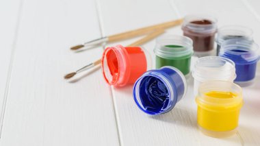 İki fırçalar ve beyaz ahşap bir masa üzerine guaş sekiz kavanoz. Yaratıcı kiti. Hobi ve stil.