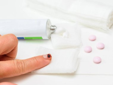 Bir bıçak kesim işaret parmağı ile sol el, bir tüp merhem ve beyaz ahşap bir masa üzerinde bir bandaj. Bir iç durum elinde zarar.