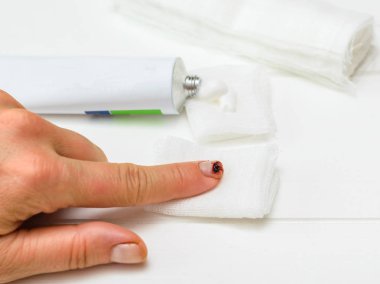 Bir bıçak kesim işaret parmağı ile sol el, bir tüp merhem ve beyaz ahşap bir masa üzerinde bir bandaj. Bir iç durum elinde zarar.