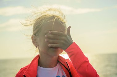 Bir kız parlak güneşin sahilde eliyle gözlerini kapamaz. Çocuk için deniz.