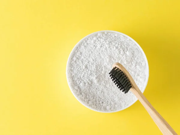 Bir kavanoz Diş tozu ve ahşap bir fırça ile sarı bir arka plan üzerinde siyah kıllar. Ağız bakım ürünleri. Üstten görünüm. Düz yatıyordu.
