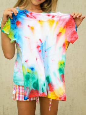 Girl trying on a t-shirt painted in the style of tie dye. White clothes painted by hand. clipart