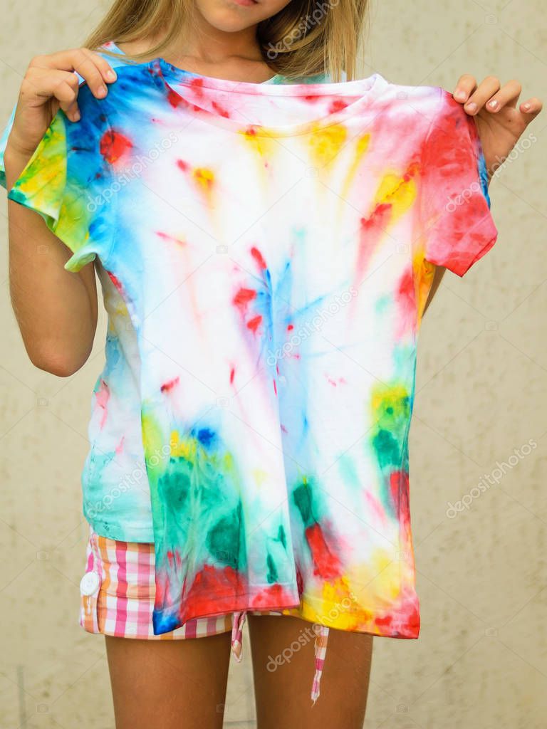 Girl trying on a t-shirt painted in the style of tie dye. White clothes painted by hand.