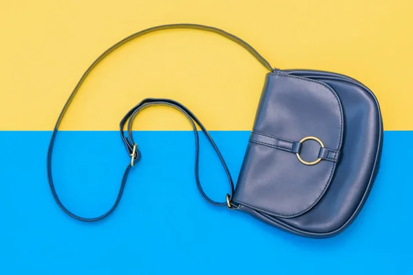 Beautiful women bag of blue leather on yellow and blue background. Women\'s accessories on colored background. The view from the top. Flat lay.