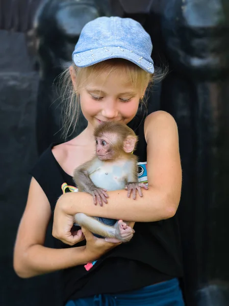戴着蓝帽子的女孩和一个小猴子一起玩耍 有猴子的女孩的照片 — 图库照片
