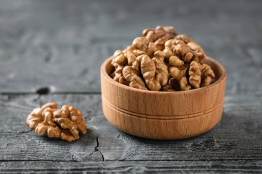 Koyu ahşap bir masa üzerinde ahşap bir kasede soyulmuş ceviz parçaları. Doğal ve diyet gıda.