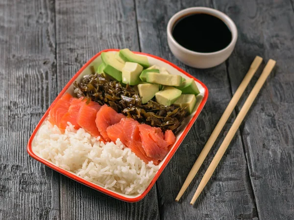Hawaii pirinç, avokado, somon ve yosun ve soya sosu siyah ahşap bir masa üzerinde bir tabak. Akdeniz diyeti mutfağı. Üstten görünüm.