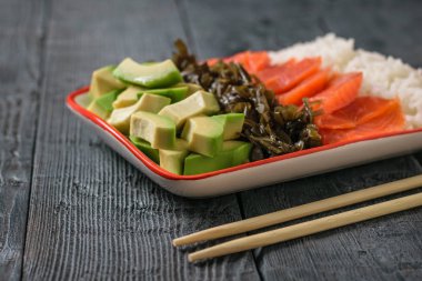 Hawaii pirinç, avokado, somon ve kelp siyah ahşap bir masa üzerinde bir tabak. Akdeniz diyeti mutfağı. Üstten görünüm.