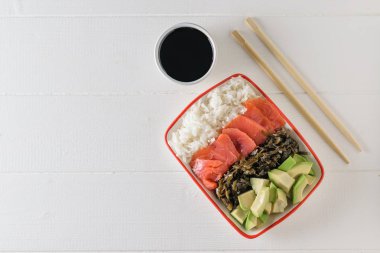 Kase uzun taneli pirinç, deniz yosunu, avokado dilimleri, bir beyaz tahta masada somon ve ahşap sopa ile. Akdeniz diyeti mutfağı. Üstten görünüm. Düz yatıyordu.