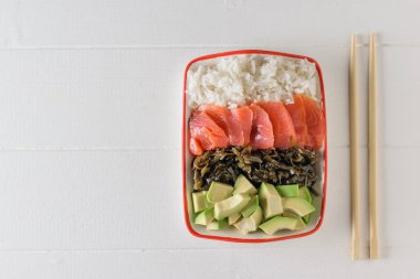 Kase uzun taneli pirinç, deniz yosunu, avokado dilimleri, bir beyaz tahta masada somon ve ahşap sopa ile. Akdeniz diyeti mutfağı. Üstten görünüm. Düz yatıyordu.