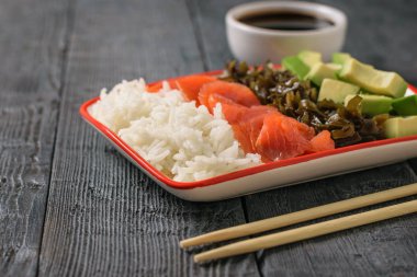Hawaii pirinç, avokado, somon ve yosun ve soya sosu siyah ahşap bir masa üzerinde bir tabak. Akdeniz diyeti mutfağı. Üstten görünüm.
