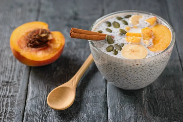 Half a peach and a wooden spoon next to a glass bowl of Chia seed pudding. Diet food for weight loss and cleansing the body.