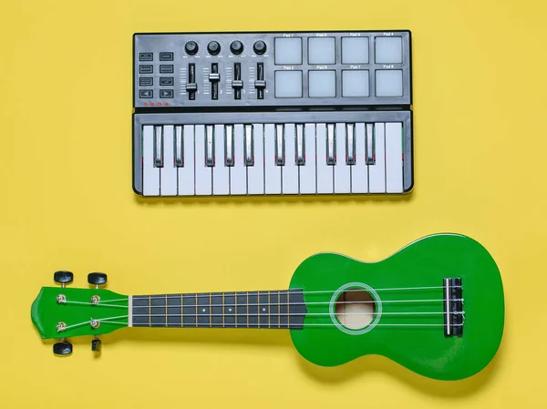 Green ukulele and music mixer on yellow background. Equipment for recording music tracks. The view from the top. Flat lay.