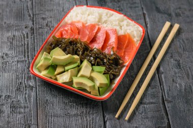 Pirinç, deniz yosunu, avokado dilimleri ve balık ahşap sopa ile siyah bir tabloda bir kase. Akdeniz diyeti mutfağı. Üstten görünüm.