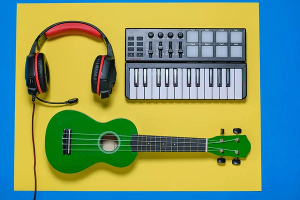 Music mixer, green ukulele guitar and red headphones on yellow and blue background. Equipment for recording music tracks. The view from the top. Flat lay.