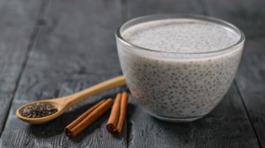 Bir cam kase, tahta kaşık ve tarçın siyah ahşap bir masa üzerinde siyah Chia tohum puding. Diyet gıda kilo kaybı ve vücut temizliği için.