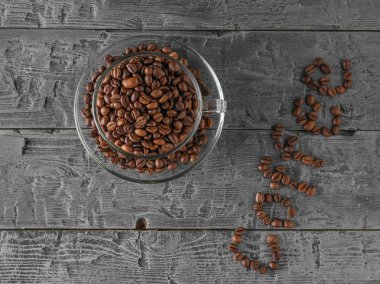 Bir fincan kahve çekirdekleri ve kahve yazıt üzerinde siyah bir ahşap masa kahve çekirdekleri ile kaplı. Üstten görünüm. Düz yatıyordu. Taneleri popüler içki hazırlanması için. Düz yatıyordu.