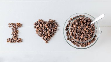 Beyaz ahşap bir masa üzerinde kahve çekirdekleri ile kaplı seviyorum yazıt. Üstten görünüm. Düz yatıyordu. Taneleri popüler içki hazırlanması için.