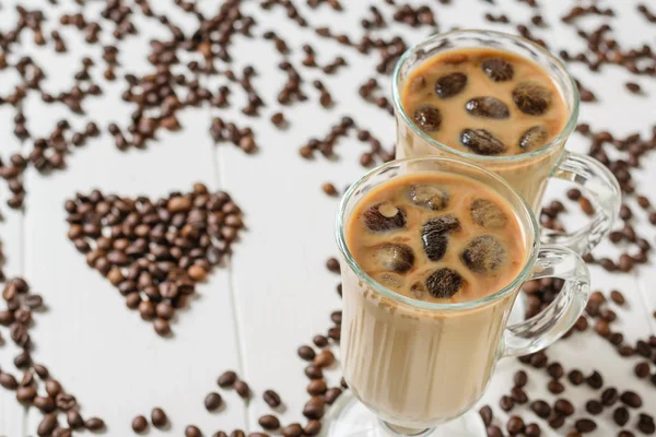 Two glasses with ice coffee and cocktail tubes on the background of the heart of coffee beans. Refreshing and invigorating drink of coffee beans and milk.