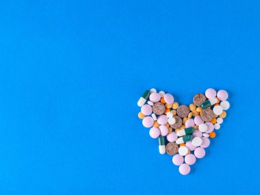 Kalp mavi arka plan üzerinde renkli hapları yapılmış. Üstten görünüm. Tedavi ve hastalıkların önlenmesi kavramını. Düz yatıyordu.