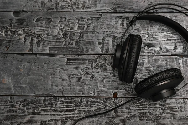 Black headphones with wire on black wooden table. The view from the top. Equipment for music Studio. Flat lay.