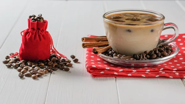 A red bag filled with coffee beans and a Cup of ice coffee and cinnamon on a white table. Refreshing and invigorating drink of coffee beans and milk.