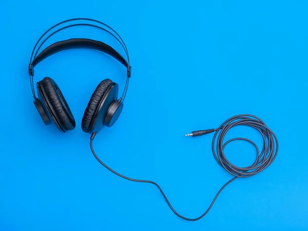 Black headphones with coiled cord on blue background. Accessory for listening to music and communication.