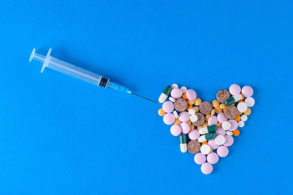 The syringe needle gets to the heart of pills on a blue background. The view from the top. The concept of treatment and prevention of diseases. Flat lay.