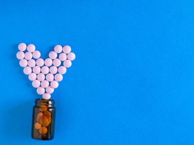 Pembe hap kalbinde bir cam balon mavi bir arka plan üzerine dökülür. Üstten görünüm. Tedavi ve hastalıkların önlenmesi kavramını. Düz yatıyordu.