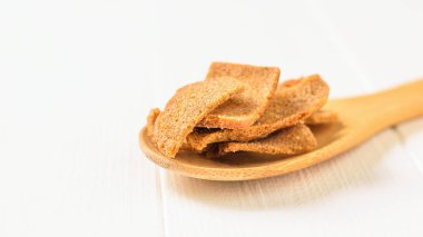 Beyaz ahşap bir masa üzerinde bir tahta kaşık otlar ile kraker. Meze baharatlar ile kuru ekmek.
