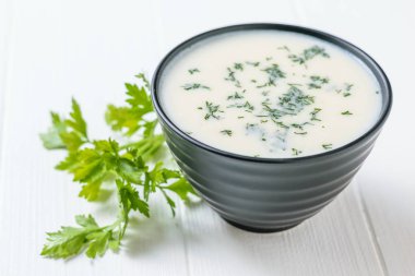 Krem karnabahar çorbası ile kase ve bir beyaz tahta masada maydanoz sapı. Keto diyet yemek.