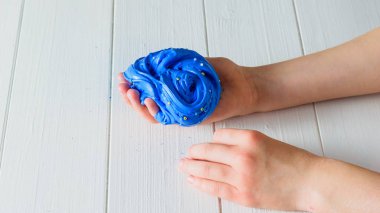 Çocuk mavi bir slayt bir beyaz tahta masa üzerinde tutuyor. Oyuncak antistress. El motor becerilerinin geliştirilmesi için oyuncak.