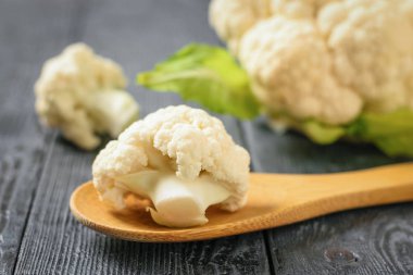 Önümüzdeki bir tahta kaşık bir koyu siyah masada karnabahar. Sağlıklı vejetaryen diyet.