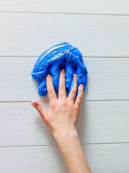 The child\'s fingers are immersed in a blue slime on a white table. Toy antistress. Toy for the development of hand motor skills.