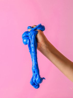 Mavi bir sümük pembe bir arka plan üzerinde bebeğin elinden aşağı akar. Oyuncak antistress. El motor becerilerinin geliştirilmesi için oyuncak.
