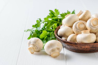 Maydanoz bir kil kase taze mantar beyaz bir masada bırakır. Vejetaryen mutfağı.