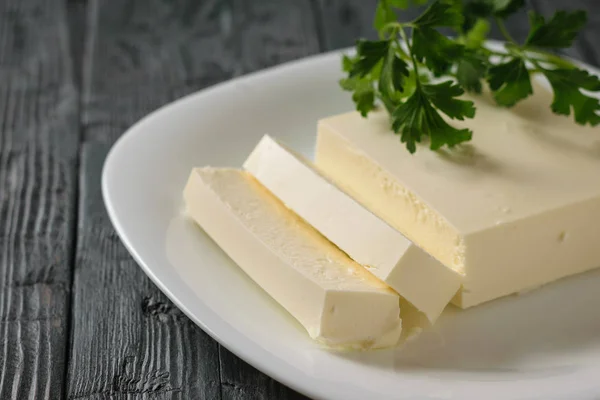 Cut Serbian cheese with parsley leaves in a bowl on a wooden table. The view from the top. Dairy product.