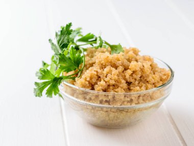 Maydanoz yaprakları ile beyaz bir tabloda bir cam kase pişmiş quinoa tahıl. Bir haşlanmış mısır gevreği glutensiz yemek. Sağlıklı vejetaryen diyet.