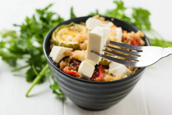 Un trozo de queso en un tenedor y un tazón de ensalada en la mesa. Plato vegetariano . — Foto de Stock