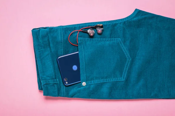 Навушники та телефон у кишені з зелених джинсів на рожевому фоні . — стокове фото
