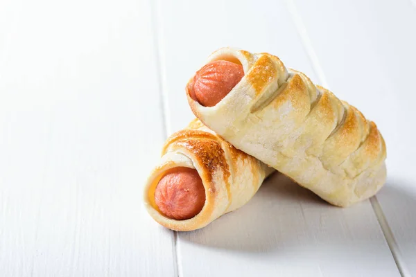 Two fresh sausage rolls on a white rustic table.