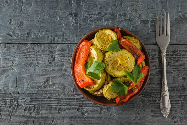 Un tazón de verduras horneadas y un tenedor sobre una mesa de madera negra. Plato vegetariano. Alimento vegetal natural. La vista desde arriba . — Foto de Stock