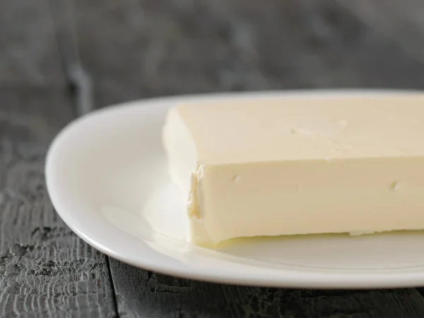 Un trozo grande de queso en un plato blanco sobre una mesa negra. La vista desde arriba. Productos lácteos . —  Fotos de Stock