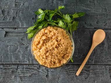 Siyah ahşap bir masa üzerinde bir kaşık ile cam kase haşlanmış quinoa. Üstten Görünüm. Düz yatıyordu.
