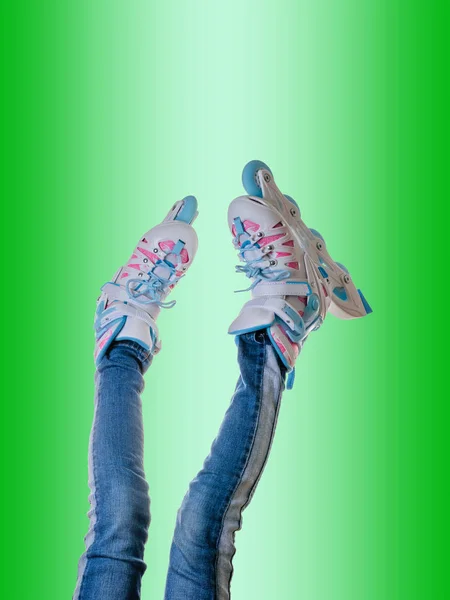 Baby feet in roller skates and jeans on green background. — Stock Photo, Image