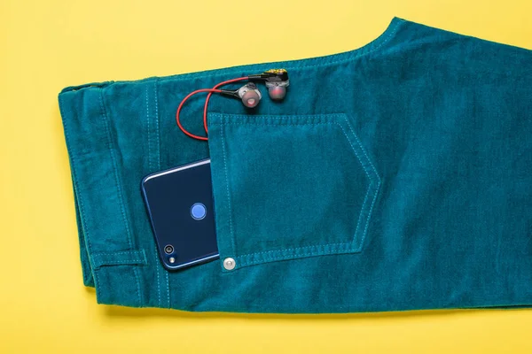 Синій телефон стирчить з кишені зелених джинсів на жовтому фоні . — стокове фото