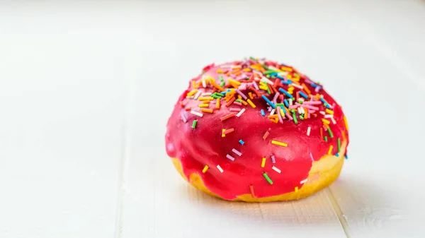 Beautiful fresh donut in red glaze on white wooden table.