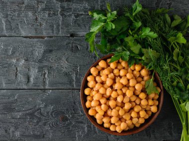 Siyah ahşap masada haşlanmış nohut ve otlar ile kil kase. Üstteki görünüm.