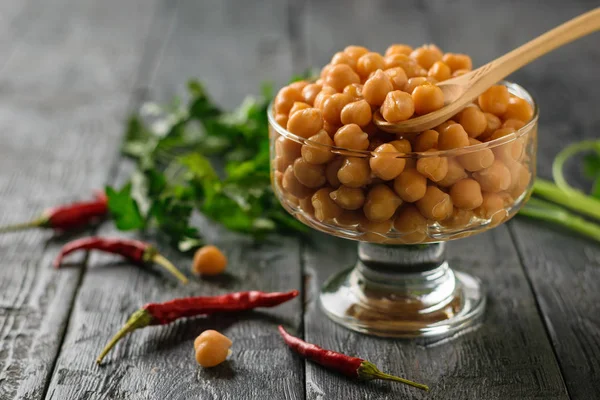 Siyah bir masada biber ve otlar ile haşlanmış nohut ile bir cam kase ahşap kaşık.